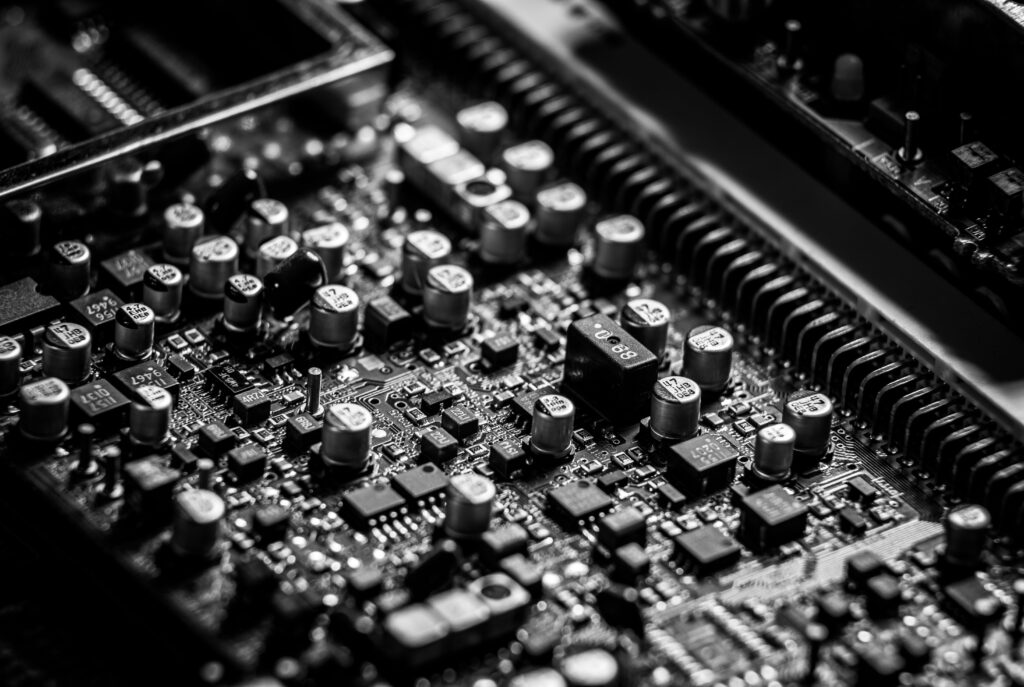 Detailed black and white close-up of an electronic circuit board, highlighting capacitors and microchips.